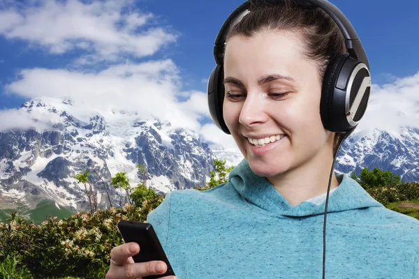 Meisje met een speler en in de koptelefoon tegen een achtergrond van een berglandschap op een heldere zonnige dag. Ontspannen in de natuur. Luisteren naar muziek in openlucht. — Stockfoto