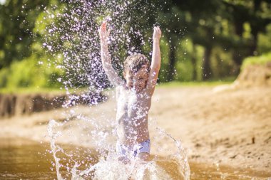 Küçük çocuk su sıçramalarına yapar ve gölde yaz aylarında düşer. Bir çocuk gölde güneşli bir günde yıkıyor.
