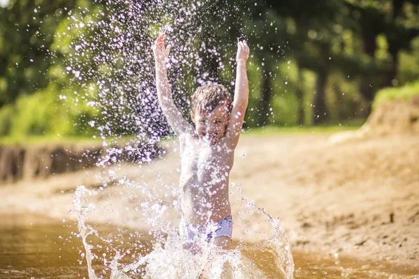 El niño hace salpicaduras y gotas en el lago en verano. Un niño se baña en el lago en un día soleado — Foto de Stock