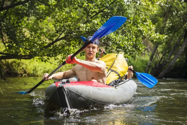 Kayaking on river. Athletic guys in canoe rowing with oars. Active recreation in nature. Water adventure. Rafting on river. Two friends in kayak with oars. Men are swimming along river in a kayak