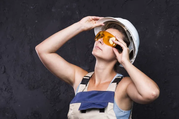 De werknemer van de bouwer van het vrouw in uniform met witte helm en beschermende constructie bril op zwarte achtergrond. Vrouw in werkkleding — Stockfoto
