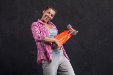 Elinde bir kaykay ile moda güzel bir genç kız portresi. Şık elbiseleri gülümseyen bir kız bir paten tutar. Genç modern bir kadın portresi stüdyo