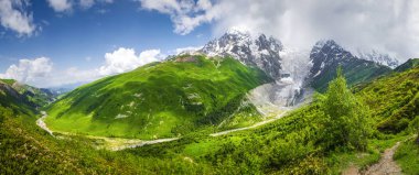 Güneşli yaz gününde inanılmaz Svaneti dağ manzarası. Gürcistan'daki Mount Tetnuldi ve buzul Lardaad, yeşil çimenli hills, dağ nehir. Mavi gökyüzü ve bulutlar dağlar trek üzerinden. Adishi'da yürüyüş.
