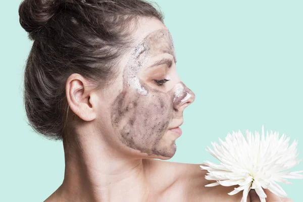 Perawatan kulit. Wanita dengan masker wajah hitam dan bunga putih — Stok Foto