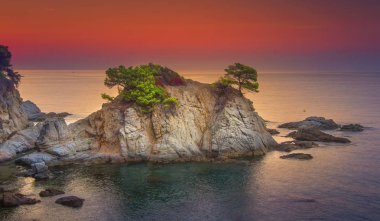 Sea landscape at sunrise. Beautiful view of cliff in Mediterranean at dawn in morning. Bright red sky over Spanish coast of Lloret de Mar, Costa Brava, Spain. Amazing nature and coastline with rocks. clipart