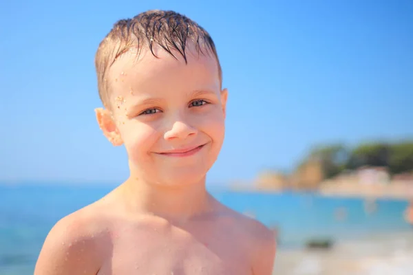 Retrato de niño blanco sonriente sobre fondo azul mar y playa en claro día soleado. Niño en la playa de Fenals platja en Lloret de Mar, Costa Brava, España — Foto de Stock