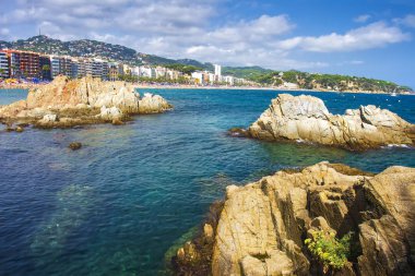 Bir Lloret de Mar güneşli yaz günü, Costa Brava, İspanya görüntüleyin. Lloret beach civarındaki deniz kayalarda. Deniz sahil şeridi üzerinde resort city ile. İspanyol tatil tatil