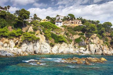 Kayalık sahil şeridi içinde Akdeniz Lloret de Mar, Costa Brava, İspanya ile köy tepeler ve dağ evleri. Güzel manzara ev deniz kıyısında buzlu. Akdeniz'in hayat yaz gününde.