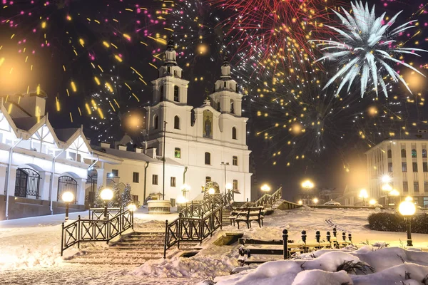 Saludo festivo en la noche Minsk para Navidad y Año Nuevo. Celebrando el Año Nuevo en Bielorrusia. Fuegos artificiales y saludos, luces de noche de la ciudad en la iglesia ortodoxa principal del espíritu santo en el centro de la ciudad . — Foto de Stock