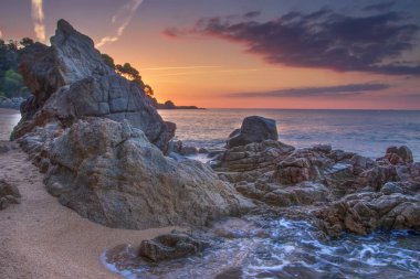 Kayalar ve taşlar üzerinde gündoğumu kumsalda muhteşem deniz manzarası. Şafak pastoral Akdeniz doğaya Lloret de Mar Beach güzel renkli gökyüzü. Manzara plaj Cala sa Boadella plaja buzlu.