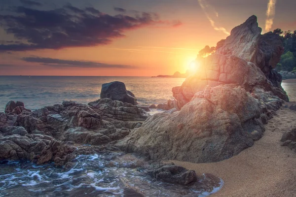 Levande soluppgång på havet med klippor och stenar på stranden. Levande landskap av havet. Marinmålning av steniga stranden i gryningen. Fantastisk utsikt över Cala sa Boadella stranden i Lloret de Mar, Costa Brava, Spanien. Ljusa solen. — Stockfoto