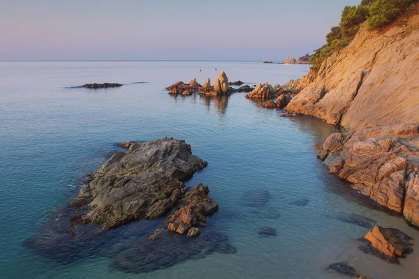 A kövek és sziklák a strand reggel elemzéséhez. Csodálatos kilátás a tengerre és a homokos tengerpart Cala sa Boadella platja Lloret de Mar: sunrise. Táj tengerpartja, a Costa Brava, Spanyolország — Stock Fotó