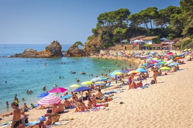 Bir Lloret de Mar, Costa Brava, İspanya - Ağustos 22, 2018: turist ile tropikal plaj. Platja de Fenals kumsalda güneşlenmek. İspanyol resorts Akdeniz sahil şeridi üzerinde. Denizde güneşli günde dinlenme.