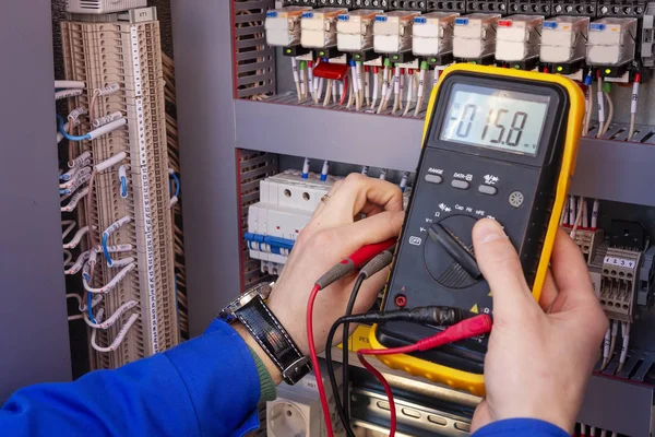 Multimeter in hands of electrician engineer in electrical cabinet. Maintenance of electric system. Worker tests of electrical circuit. Electrician with tester in hands. — Stock Photo, Image