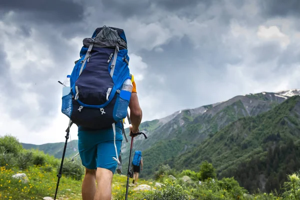 Turistik dağ Trek sırt çantası zammı ile. Svaneti, Gürcistan'da yürüyüş. Dağlarda trekking. İki adam çimenli tepe üzerinde yürümek. Boş zaman etkinliği. Spor turizm. Yürüyüşçüler maceralarını. Dağcılar bağlar. — Stok fotoğraf