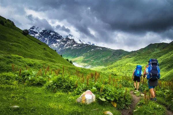 Dağlarda hiking. Sırt çantaları dağ turistlerle. Svaneti bölgesi, Georgia trekking. İki adam bağlama izi yürüyüş. Gürcü çimenli tepeler ve rocky Dağları kar ile spor turizm. — Stok fotoğraf