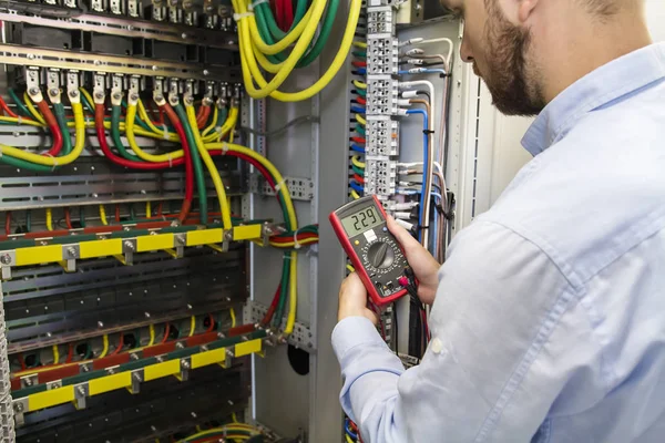 Ingeniero electricista prueba conexión de cableado de línea eléctrica de alta tensión en tablero de fusibles de distribución industrial. Hombre de servicio con multímetro. Probador en manos del trabajador eléctrico . — Foto de Stock