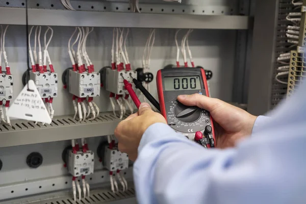 Multímetro en manos del electricista de cerca. El servicio funciona en caja eléctrica. Mantenimiento del panel eléctrico. Técnico probando caja de fusibles de voltaje. Trabajador con probador — Foto de Stock