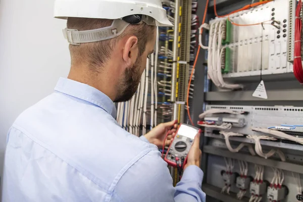 Unga vuxna elektriker builder ingenjör inspektera elektrisk utrustning i distribution säkringsdosan. Elektroingenjör arbetaren i Kontrollpanelen. Underhåll elektronisk låda med multimeter — Stockfoto