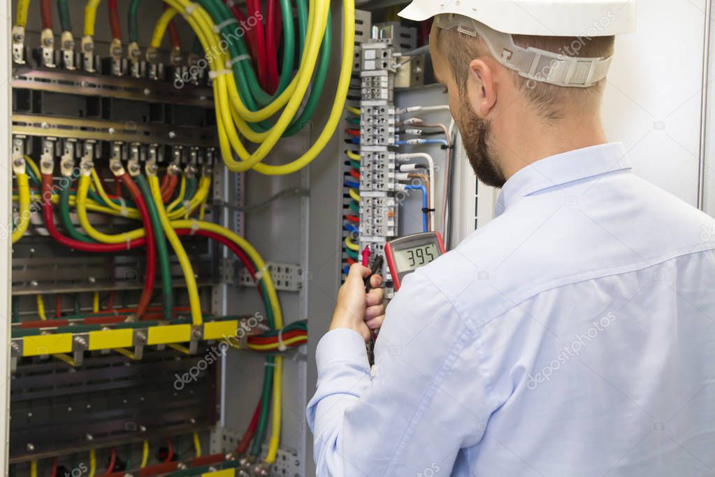 Electrician engineer at work inspecting cabling connection of high voltage power electric line in industrial distribution fuseboard. Service man with multimeter