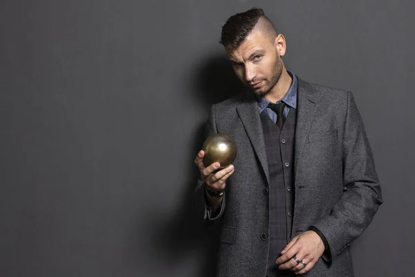 Handsome man in suit holds in hand golden ball. Elegant man business teacher. Fashionable and stylish confident man