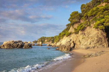 Lloret de Mar. Cala de Boadella platja, İspanya, Costa Brava güzel İspanyol Beach'te. Manzara plaj sabah güneş ışığı altında. Sandy plaj sahil şeridi üzerinde taşlarla. Deniz manzarası. Pastoral deniz kıyısında. Deniz doğa.