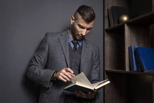 Aantrekkelijke man in een pak leest een boek. De advocaat houdt de directory in zijn kantoor. Leren man met boek. Zelfverzekerde man in bibliotheek. — Stockfoto