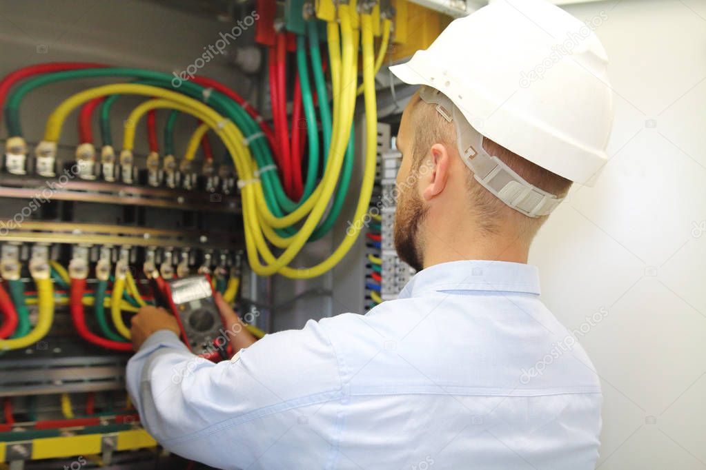 Electrician at work measures voltage in industrial distribution fuseboard