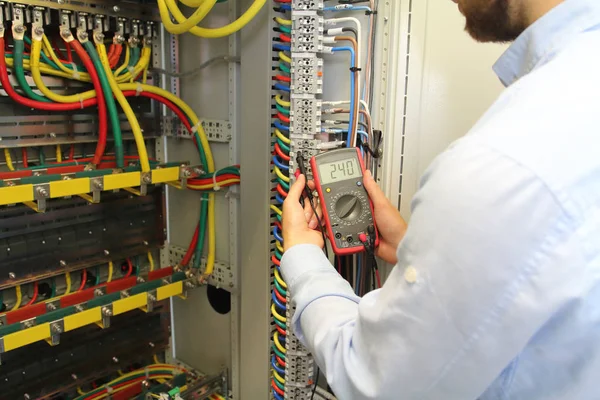 Elektricien werkt in elektriciteitskabels distributie zekeringenkast met multimeter — Stockfoto