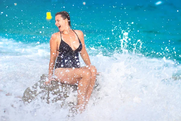 Весела дівчина на морському пляжі з бризками води з хвиль — стокове фото