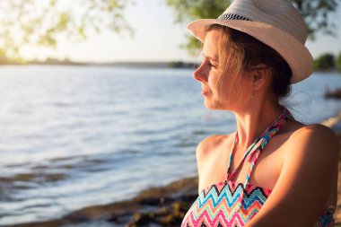 Göl kenarında şapkalı güzel kız mesafe içine bakar ve gün batımında rüyalar