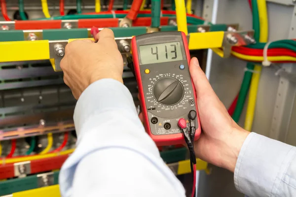 Electrician uses multimeter in fuse box. Engineer measuring voltage in electrical cabinet. — Stock Photo, Image