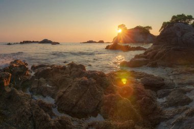 Gün doğumunda deniz kayalık plaj manzara. İspanyol sahilinde güneş parlatıyor