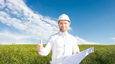 Beyaz miğfer takan mimar yeşil alan arka planı projesinin başlamasını tebrik ediyor. Mimar, planlarda dilencilik projesinden memnun. Başarılı iş.