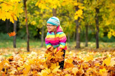 Arka planda kal. Mutlu çocuk. Düşen yapraklarla oyun. Kız gülümsüyor ve dökülen yaprakları atmaya başlıyor. Sonbahar yaprakları dökülüyor.