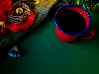 Kırmızı bir kahve fincanı yeşil bir yüzeye oturur. Kadehin etrafı şenlikli süslemelerle dolu.,