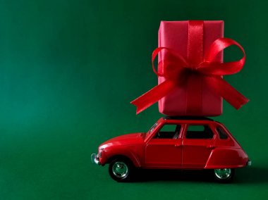 Kırmızı kurdeleli hediye kutusu olan kırmızı oyuncak araba yeşil bir yüzeye oturur.. 