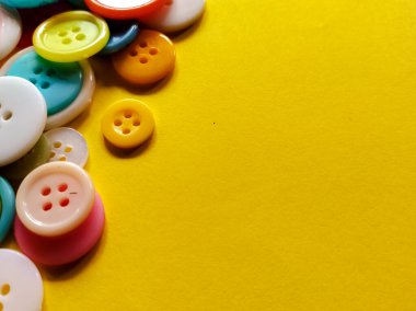 A collection of colorful, round plastic buttons is scattered on a bright yellow background. 