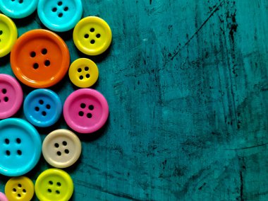 Colorful sewing buttons are clustered on a textured teal surface. 