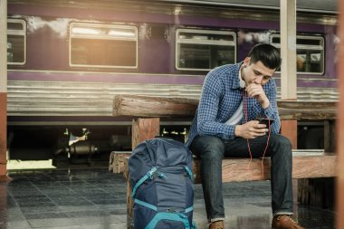Genç adam akıllı telefon tutarak ve bekleyen tren istasyonu ile müzik çalma listesi kullanma.