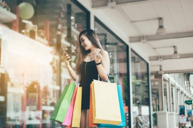 Asyalı kadın alışveriş sonra Smartphone ve dostluk mesajı kullanarak.