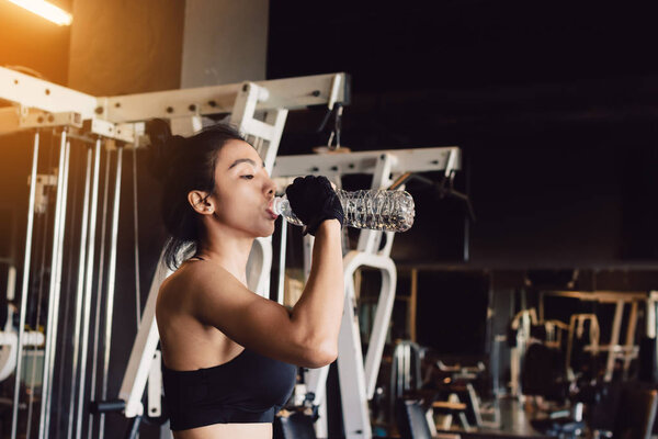 Asian young woman drinking water in the gym.