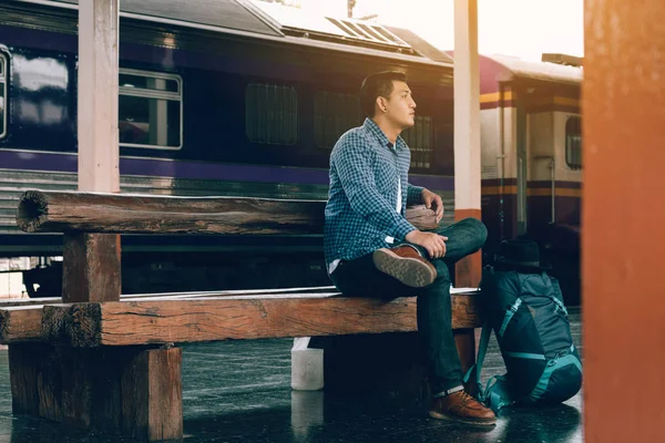 若者は列車の到着を待っていると駅で座っています — ストック写真