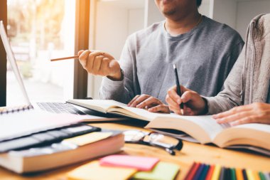 Asya genç üniversite öğrencileri birlikte kitaplığındaki masada oturan ve bilgisayar dizüstü paylaşımı.