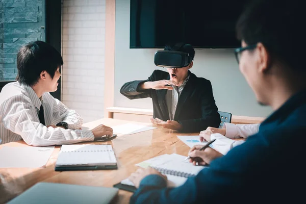 Asian business team using virtual reality VR headset in office meeting.