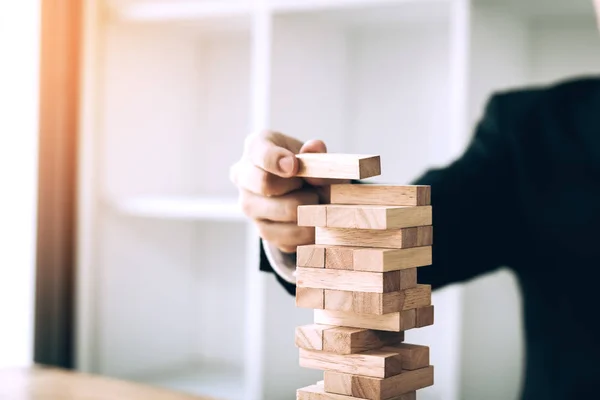 Hand of businessman playing wood blocks stacks game with planning strategy of project management.