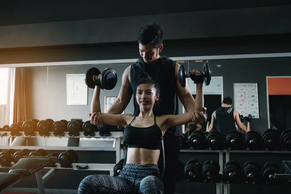 Personal trainer helping woman working lift heavy dumbbells two hand top a head.
