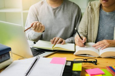 Asya genç üniversite öğrencileri birlikte kitaplığındaki masada oturan ve bilgisayar dizüstü paylaşımı.