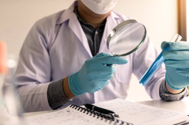 Chemist or scientist using magnifying glass looking the solution in test tube.