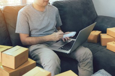 Bilgisayar dizüstü bilgisayarda bakarak ve kağıt üzerinde KOBİ kavramı sipariş listesi yazarak Genç Asyalı adam.